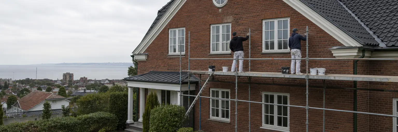 Målare på ställning vid tegelfasad i Helsingborg med Öresund i bakgrunden