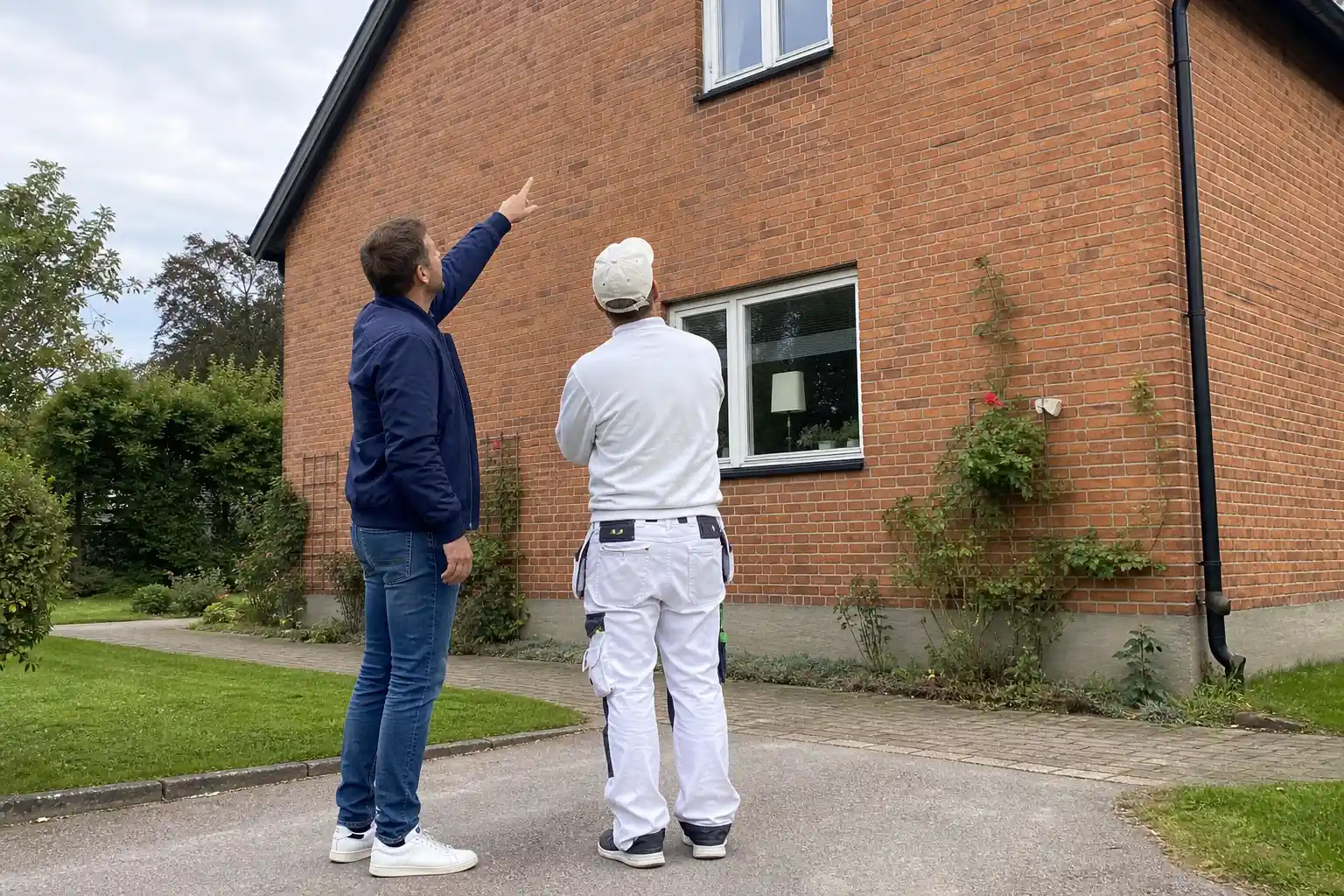 Husägare inspekterar avflagnad och missfärgad fasad på villa i Kristianstad