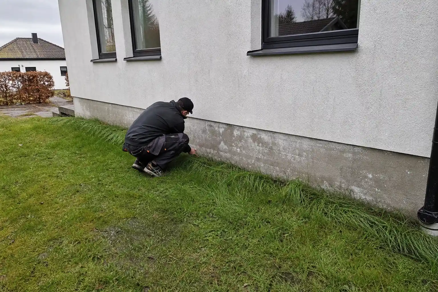 Murare undersöker en fuktskadad sockel med saltutfällningar på ett putsat hus i Kristianstad