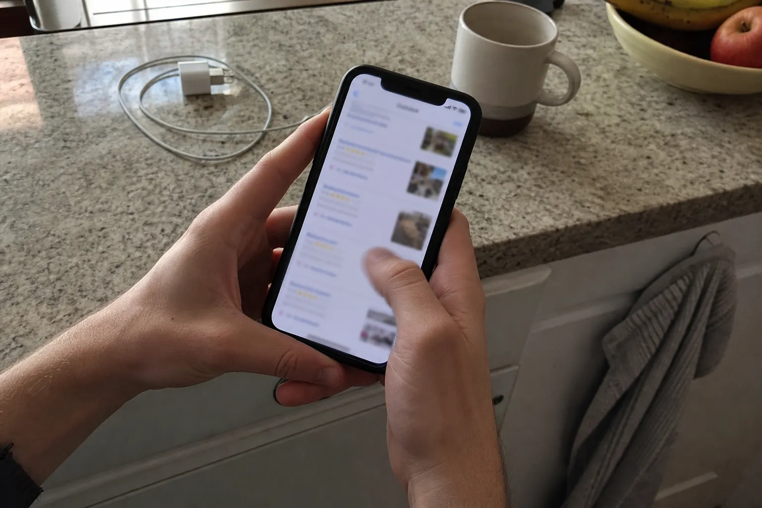 Person scrollar bland suddiga sökresultat på mobilen vid köksbänken, i jakt på fejkade hantverkarsajter.