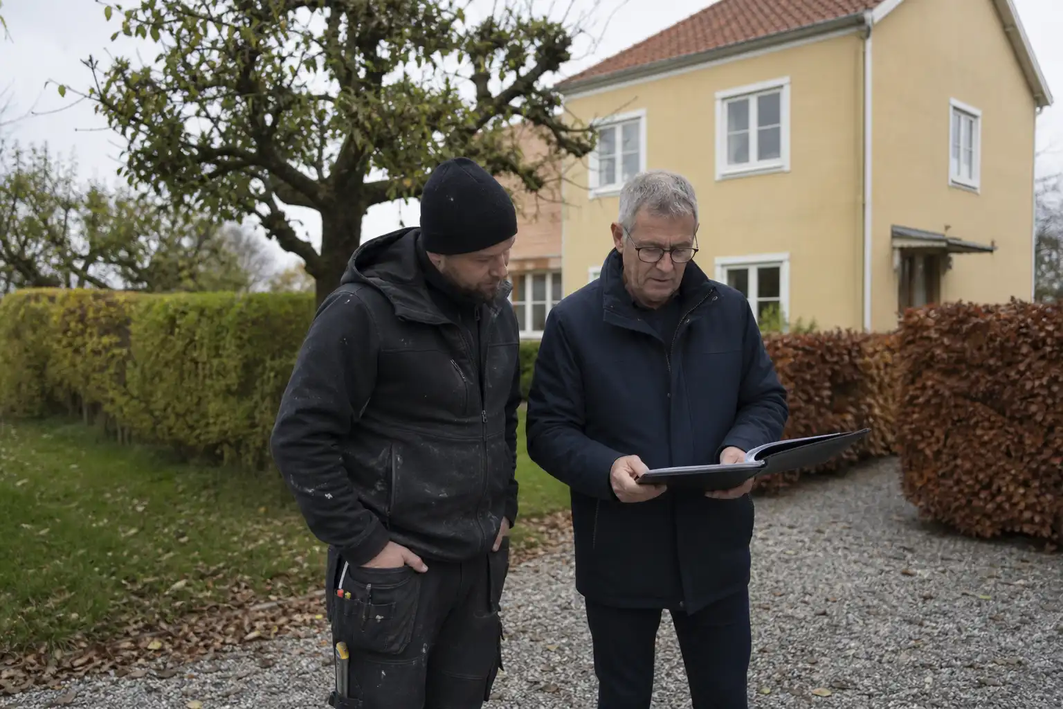 Husägare och plåtslagare läser igenom offerten framför en gul villa i Hässleholm