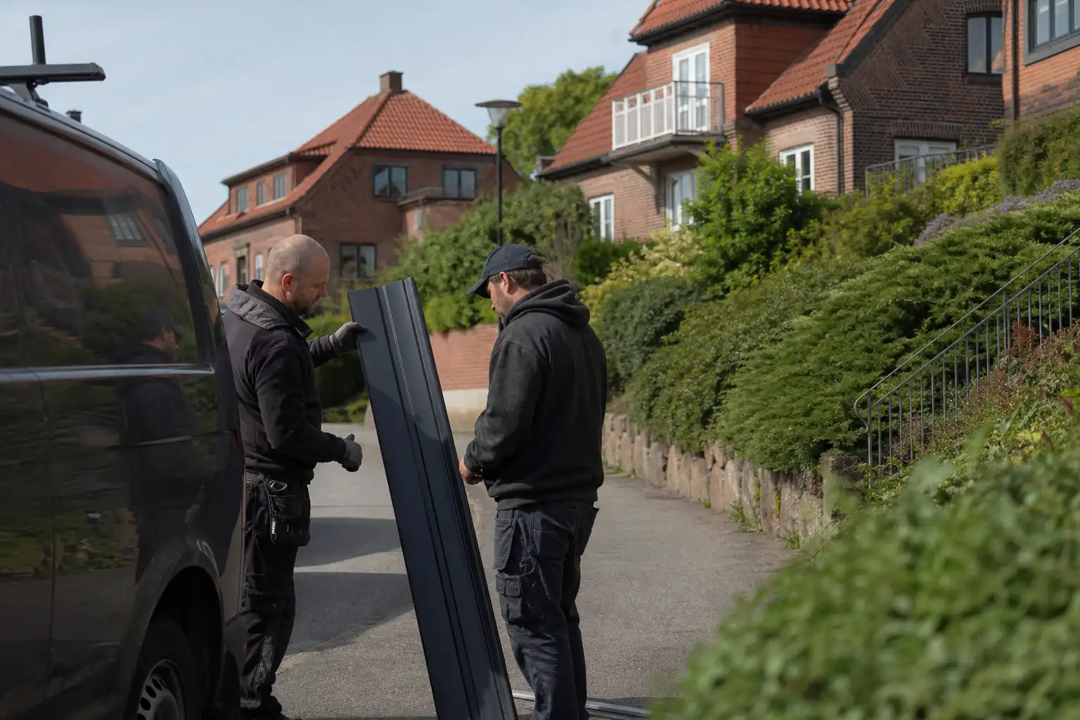Två plåtslagare lyfter av en plåtlängd vid bilen i ett villakvarter på höjden i Helsingborg