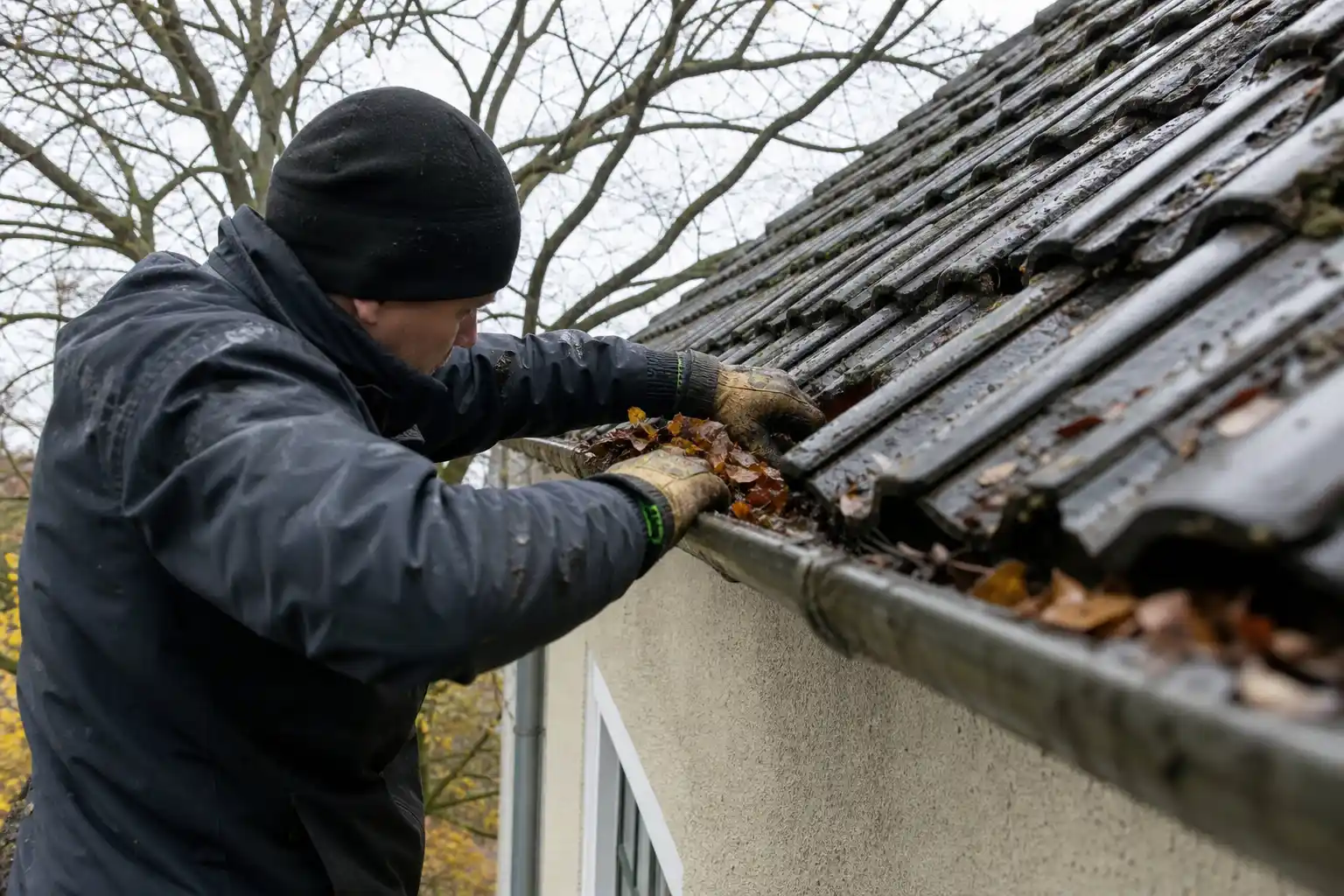 Plåtslagare rensar löv ur hängrännan på en villa i Malmö en mulen höstdag