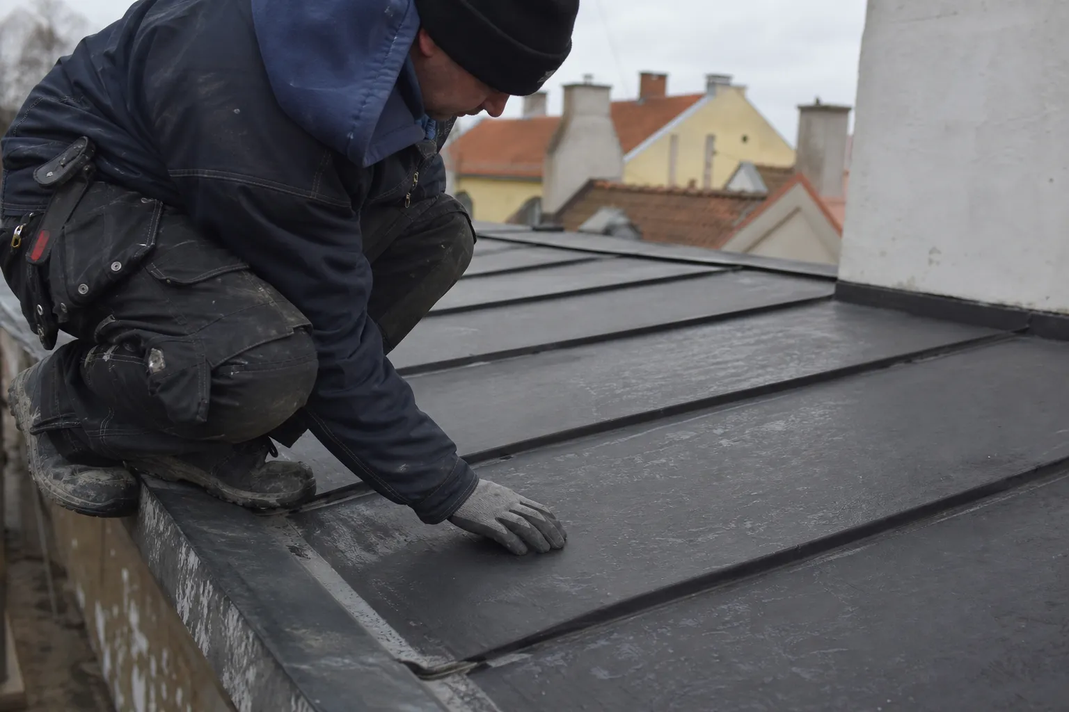 Plåtslagare känner efter längs falsen på ett flackt svartmålat plåttak i Ystads stadskärna