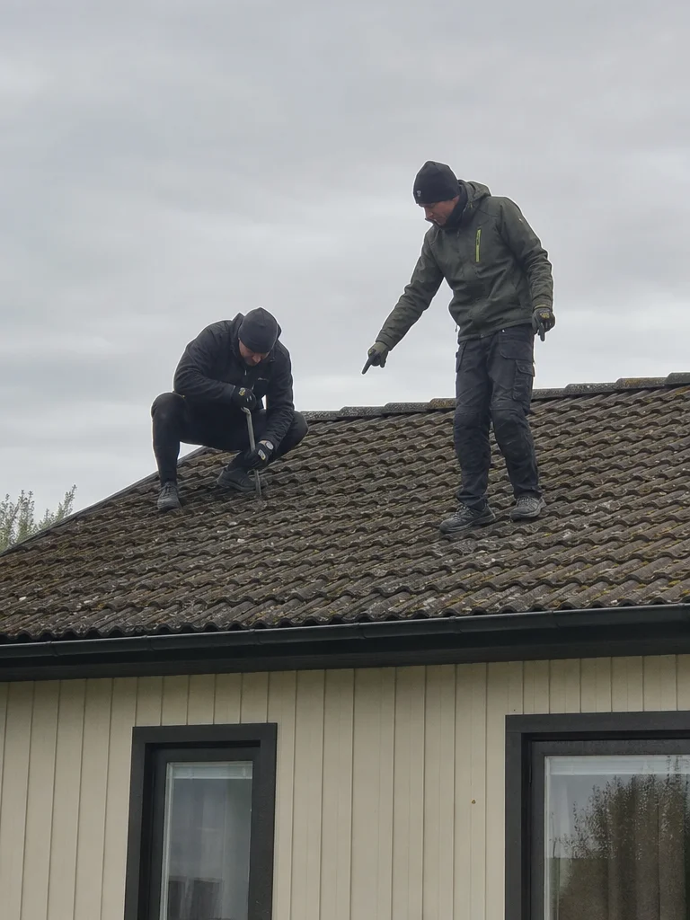 Takläggare behandlar mossbelagd betongpanna på äldre villa i Kristianstad