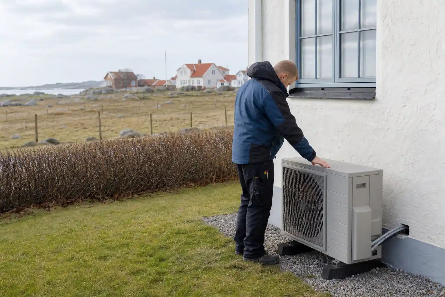 Installatör kontrollerar utedelen till en luftvärmepump vid ett putsat hus utanför Ystad